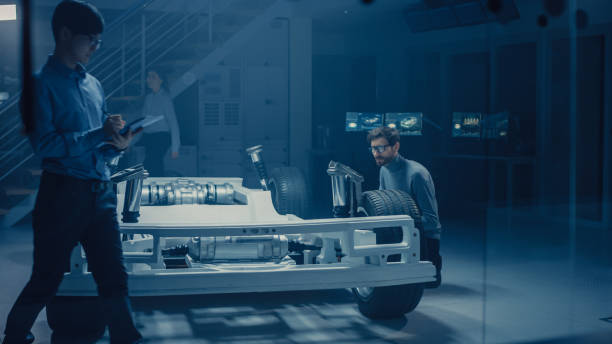 istock Automobile Design Engineer Sitting Beside Hybrid Electric Car Chassis Platform, Using Tablet Computer for Design Improvement. Facility with Vehicle Frame with Suspension, Wheels, Engine and Battery 1162762193