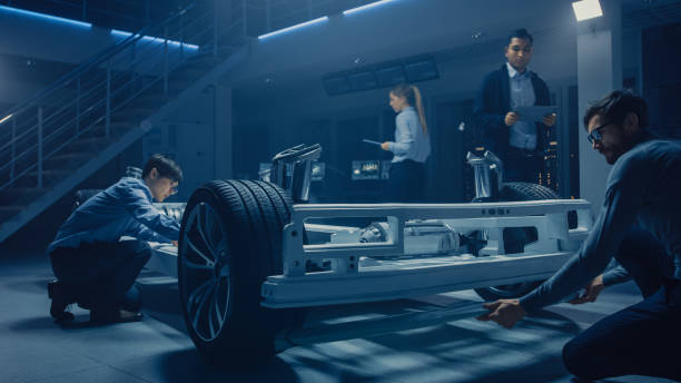 istock Team of Automotive Engineers Working on Electric Car Platform Chassis, Taking Measures, working with 3D CAD Software, Analysing Efficiency. Vehicle Frame with Wheels, Engine and Battery. 1162762293