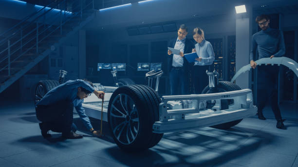 istock Team of Automotive Engineers Working on Electric Car Platform Chassis, Taking Measures, working with 3D CAD Software, Analysing Efficiency. Vehicle Frame with Wheels, Engine and Battery. 1162762343