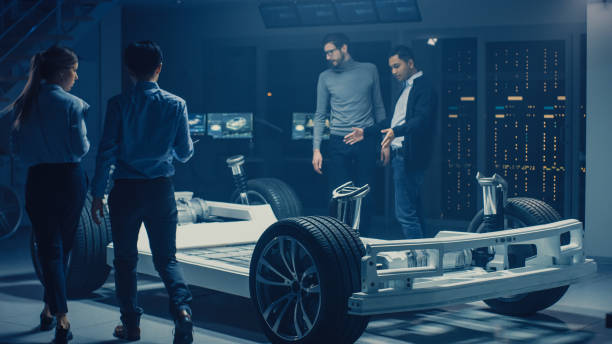 istock Team of Automotive Engineers Discussing and Designing Electric Car Platform Chassis Prototype, Taking Measures, Working with 3D CAD Software, Checking Quality Control. Vehicle Frame with Wheels, Engine and Battery. 1162762398