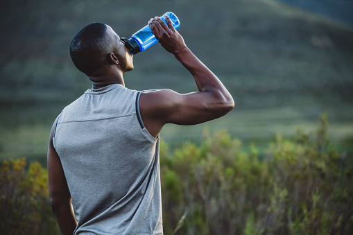Shot of a sporty young man drinking water while out for a run in nature