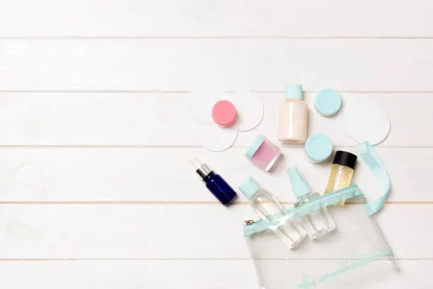 Set of travel size cosmetic bottles on white wooden table background. Flat lay of cream jars. Top view of bodycare style concept.