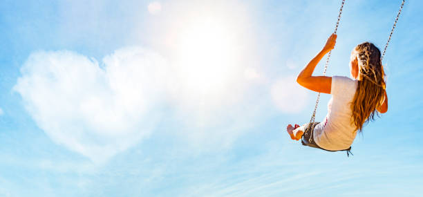 istock Woman on a swing with blue sky and heart-shaped cloud 1162786057