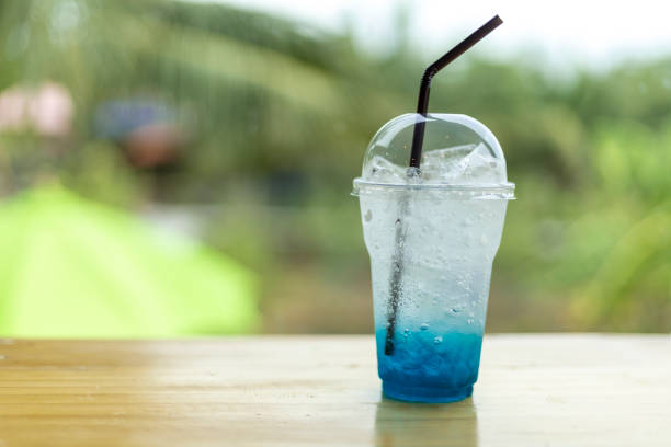 Ice blue soda in plastic cup on wooden table with green tree light bokeh background.