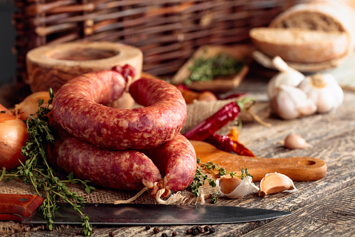 Dry-cured sausage with thyme, onion, garlic and pepper. Sausage with bread and spices on a old wooden table.