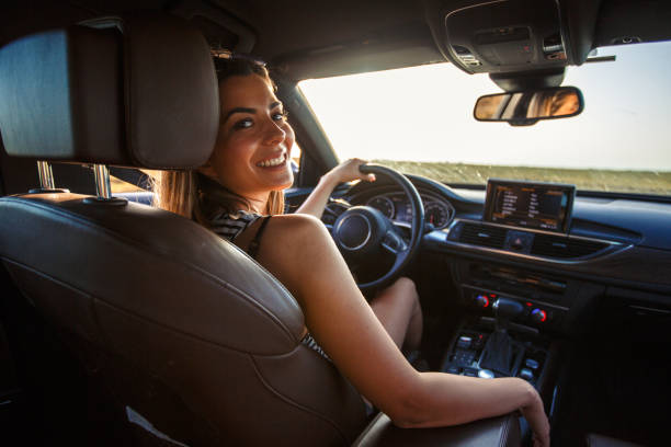 giovane donna sorridente che va in viaggio - driving women rear view sitting foto e immagini stock