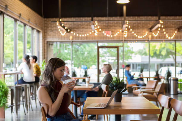 businesswoman reviews document on laptop - cafeteria imagens e fotografias de stock