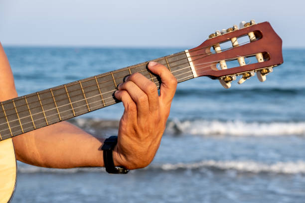 A man's hand holds a Spanish guitar neck with the sea in the background. stock photo