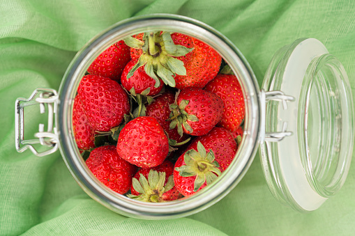 Strawberries in a glass jar on green cloth. Top view
