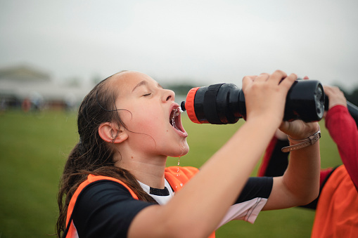 Close-up of a teenage girl squirting water into her mouth from her water bottle during a break at her football practice.