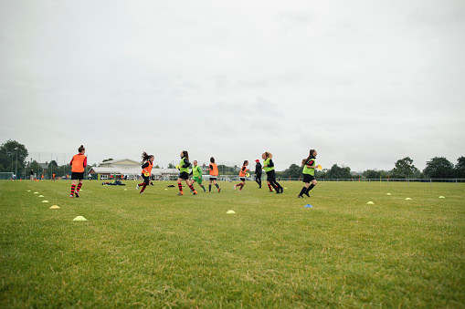 Wide angle view of a small teenage girls football club running through drills during a practice session.