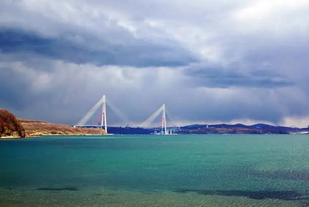 Bay by the sea with turquoise water. In the background cable stayed bridge. Stormy sky overcast. Russia, Vladivostok, island Russian
