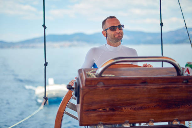 Sailor using wheel to steer rudder on a sailing boat.