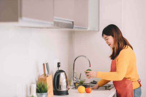 istock young woman washing vegetables at kitchen smiling 1162810875