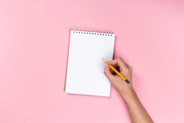 istock Woman's hands with perfect manicure holding pencil and  notepad as mockup for your design. Pink background, flat lay 1162812590