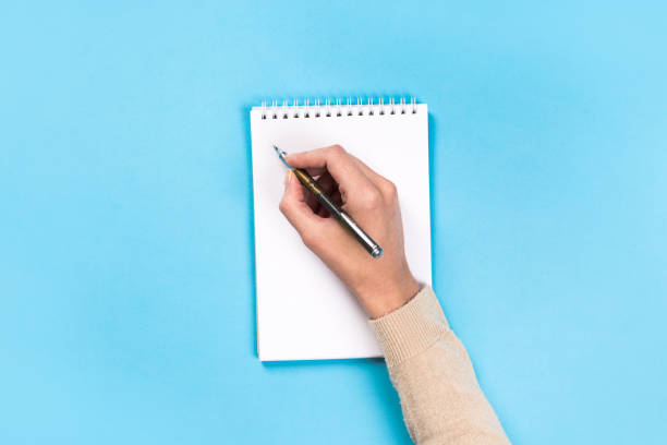 istock Woman's hands with perfect manicure holding pencil and  notepad as mockup for your design. blue background, flat lay 1162812715