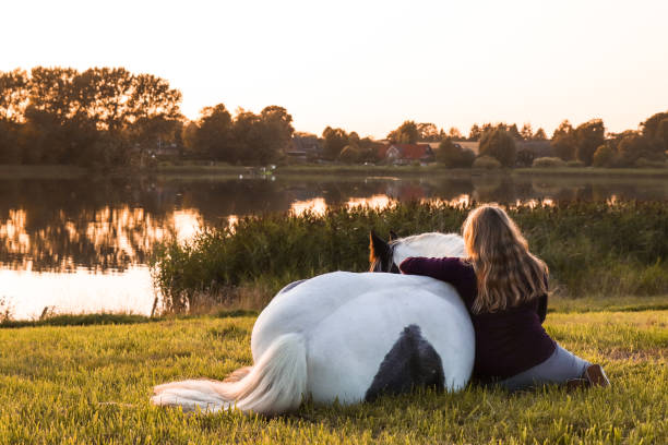 A girl and her horse sitting by the lake enjoying the golden sunset.