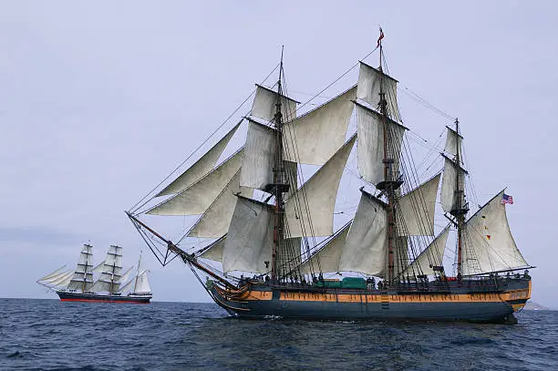 Tall ship under sail with a large ship in the background as to battle against.