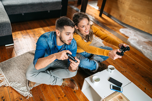 Young couple spending quality time together, playing video games, sitting on the floor, having fun