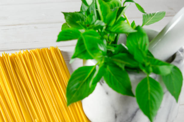 Fresh green basil in a white marble mortar on a wooden table next to pasta