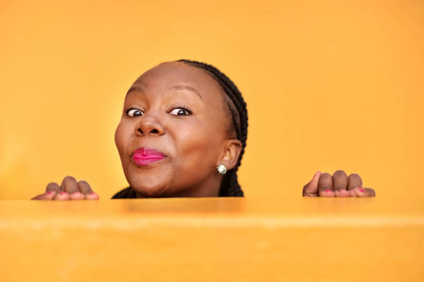 Peeking from behind a wall Shot of a funny mature woman peeking from behind a wall on yellow background peeking stock pictures, royalty-free photos & images