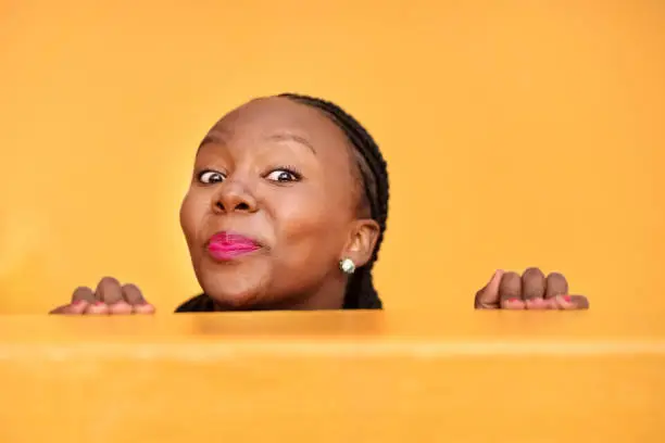 Shot of a funny mature woman peeking from behind a wall on yellow background