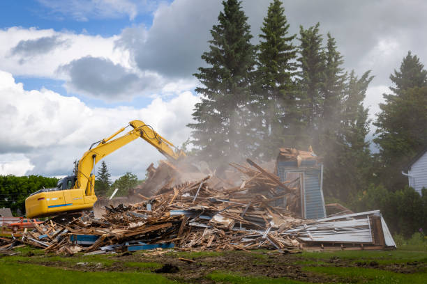 heavy duty machine demolishing a wood building horizontal image of a yellow  heavy duty  machinery tearing down and demolishing a wooden residental building with dust flying into the air at daytime in the summer. dismantling photos stock pictures, royalty-free photos & images