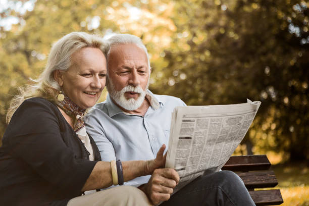 istock Senior couple relaxing outdoors reading newspaper in park 1162836865
