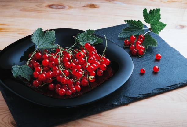redcurrants on a black plate on a wooden table stock photo