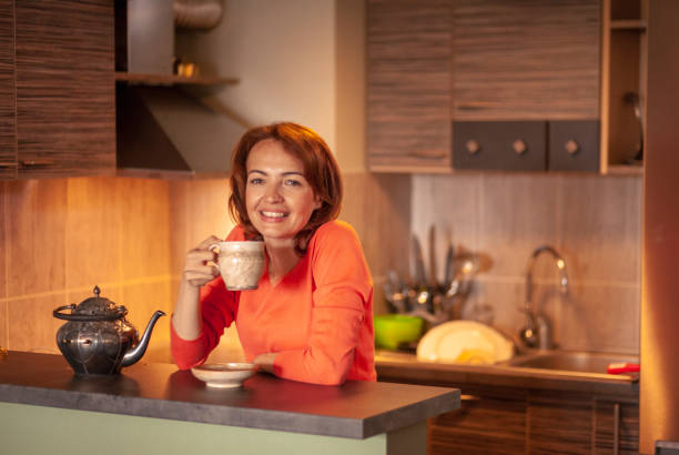 One blissful beautiful woman, 40 years old, drinking tea, relaxing in her home kitchen.