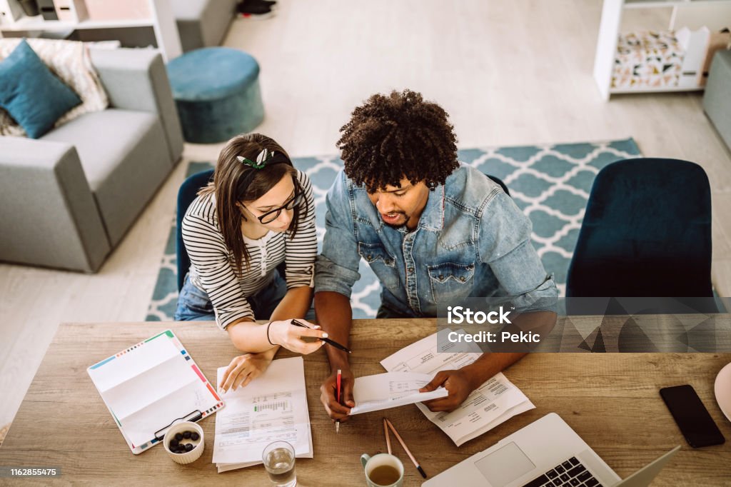 Multi-ethnic couple planning their home budget Modern married multi-ethnic young couple calculating financial bills at home Savings Stock Photo