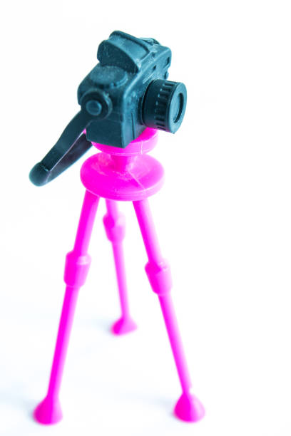 Small toy plastic camera on pink tripod close-up isolated on white background