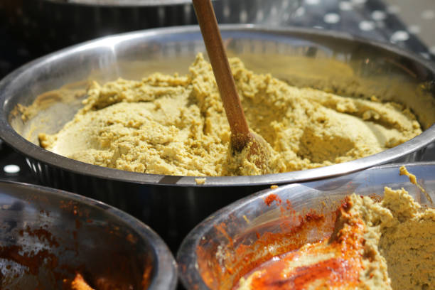 immagine del mercato dello street food con diversi tipi di hummus / pomodoro arancione houmous con spatola di cucchiaio da portata in legno, cibo della cucina greca (hommus / houmos) a base di ceci, olio d'oliva, pasta tahini e pomodori secchi al sole, in  - sesame seed spoon variation foto e immagini stock