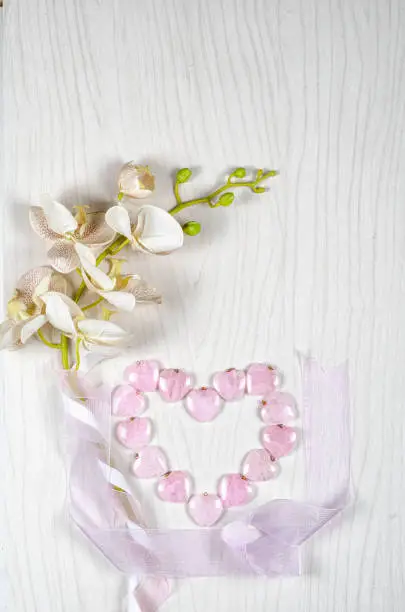 Flat lay flower and stone composition consists plastic orchid, silk ribbons and 14 rose quartz hearts which are laid out in the shape of a big heart. Top view, copy space.