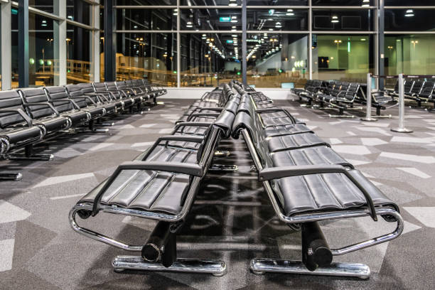 istock Empty black seats at airport gate terminal at night with reflections in large windows 1162901528