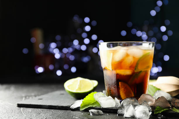 istock Glass with cola and lime slices, juicer, ice, mint against blurred lights background 1162905610