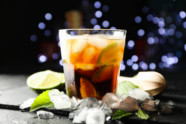 istock Glass with cola and lime slices, juicer, ice, mint against blurred lights background 1162905620