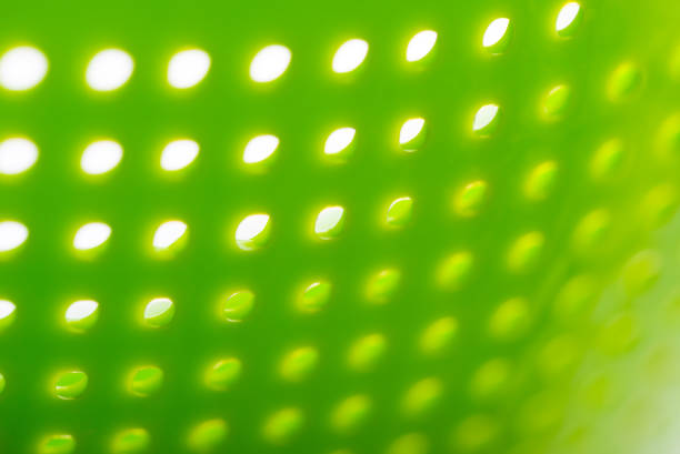 Macro of a green plastic colander, a kitchen utensil to drain pasta, on a white background, creating an abstract texture. Selective focus.