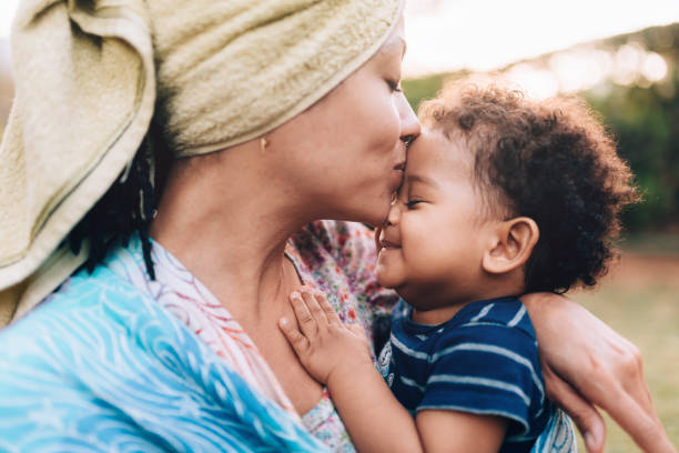 joven madre descendiente africana besando a su hijo en la frente - women mother baby happiness fotografías e imágenes de stock