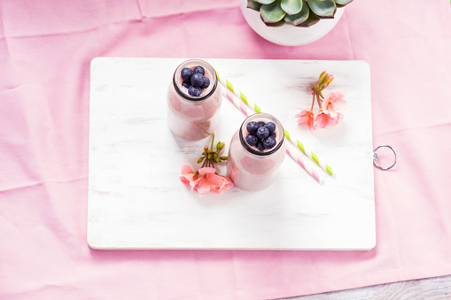 Strawberry banana smoothie topped with blueberries on pink background.