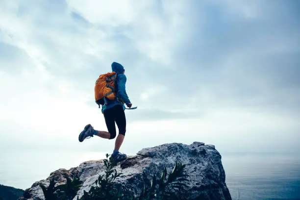 Photo of Successful woman hiker running to on seaside mountain peak cliff edge