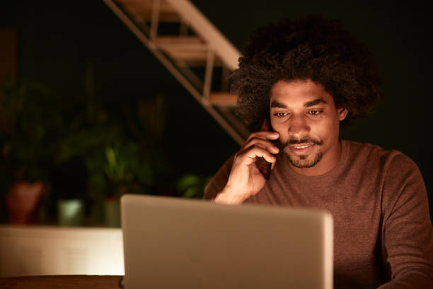 istock Young man working late at home, talking on the phone and working a laptop. 1162928082