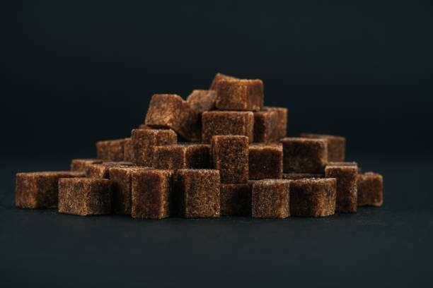 pile of unrefined brown sugar cubes on black background