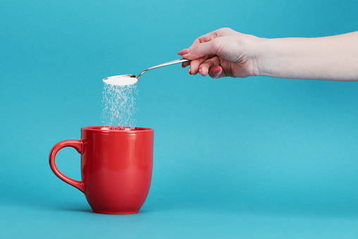 cropped view of woman adding sugar into red cup on blue background