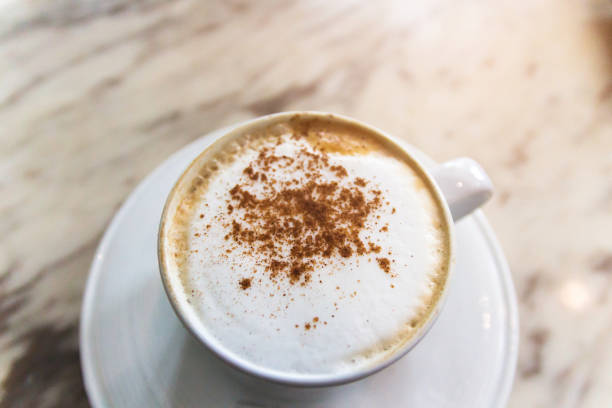 Cup of coffee with soft microfoam and cinnamon ground on marble table.