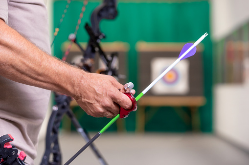 Archer holding bow picking an arrow ready to shoot to target in the background. Rear view.