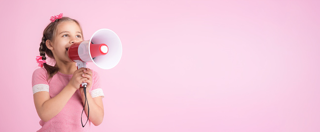 Child Girl Shouting Through Megaphone on Pink Background. Communication and Advertising Concept.
