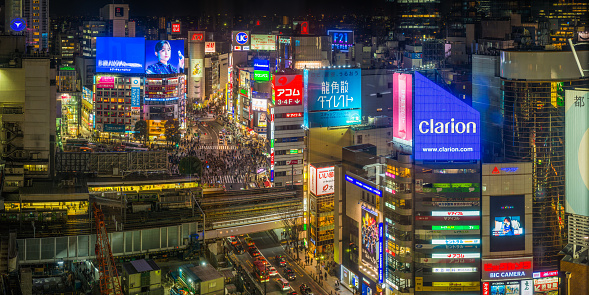 Aerial view over the iconic Shibuya Crossing and the crowds of commuters and shoppers on the streets below the colourful neon signs in the heart of Tokyo, Japan’s vibrant capital city.