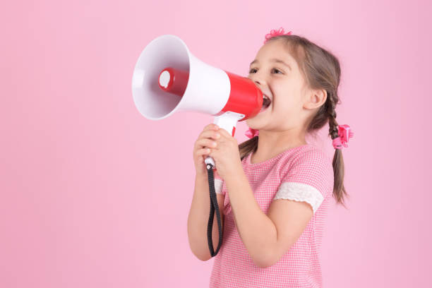 istock Child Girl Shouting Through Megaphone on Pink Background. Communication and Advertising Concept. 1162938521