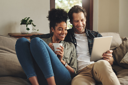 Shot of a happy young couple using a digital tablet together while relaxing on a couch at home